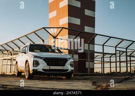 Weißes Kompakt-SUV mit Sport und modernem Design auf Betonstraße am Meer in der Nähe des Strandes bei Sonnenuntergang geparkt Stockfoto