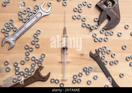 Spritze mit einem Medikament liegt auf einem Holztisch zwischen einer Vielzahl von Schraubenschlüsseln und Metallmuttern. Konzept zur Herstellung von Impfstoffen. Draufsicht. Stockfoto