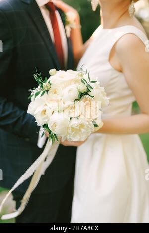 Bräutigam in einem blau karierten Anzug umarmt die Braut in einem weißen Kleid mit einem Blumenstrauß. Nahaufnahme Stockfoto