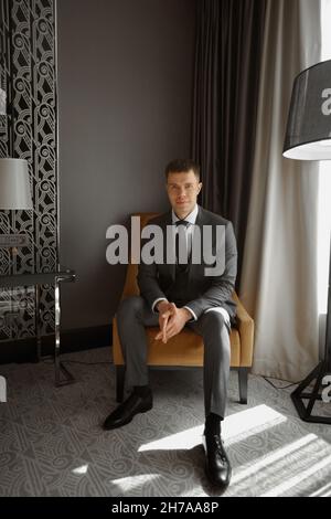 Modischer junger Mann mit Anzug im Innenraum. Hübscher junger Mann in einem klassischen Anzug, der in einem Sessel posiert Stockfoto