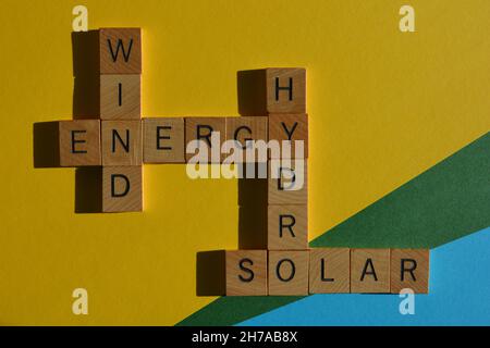 Energie, Wind, Hydro, Solar, Wörter in Holzbuchstaben in Kreuzworträtsel, isoliert auf gelbblauem und grünem Hintergrund Stockfoto