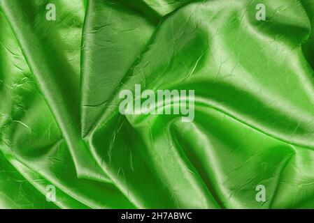 Drapierte, glänzende, faltige Seide mit einer knittergrünen Farbstruktur. Hintergrund aus gefaltetem smaragdgrünen Satin-Tuch. Edel-edles, zerknittertes Stoffmaterial. Stockfoto