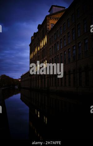 Salzmühle, entwickelt von Sir Titus Salt, in Saltaire, West Yorkshire bei Nacht, mit Fensterleuchten, die sich im Leeds - Liverpool Kanal unten spiegeln Stockfoto