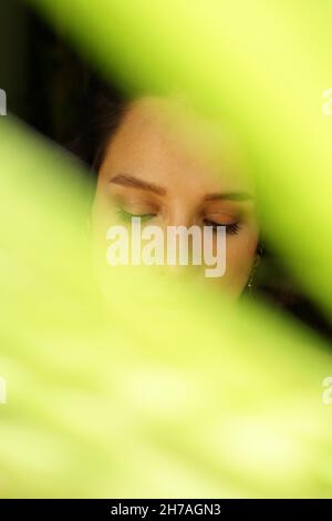 Eine vertikale Aufnahme eines jungen hispanischen dunkelhaarigen weiblichen Gesichts hinter den grünen Lichtern Stockfoto