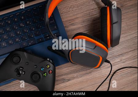 Gaming-Kopfhörer mit Mikrofon und Gamepad auf einem Laptop auf einem Holztisch. Gaming auf einem Notebook-Konzept. Draufsicht. Stockfoto
