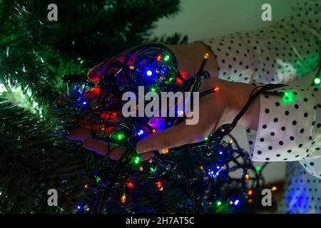 Nahaufnahme der Hände der Frau mit roten, grünen und blauen Lichtern, um den Weihnachtsbaum zu schmücken Stockfoto