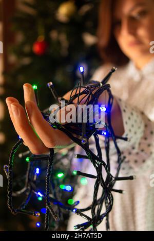 Nahaufnahme der Hände der Frau mit roten, grünen und blauen Lichtern, um den Weihnachtsbaum zu schmücken Stockfoto