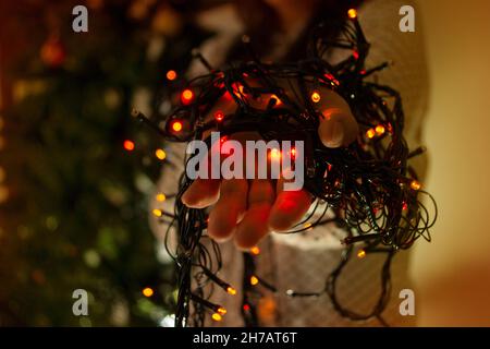 Nahaufnahme der Hände der Frau mit roten, grünen und blauen Lichtern, um den Weihnachtsbaum zu schmücken Stockfoto