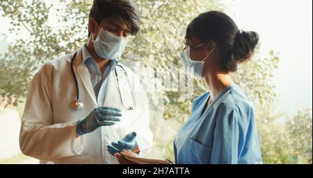 Ein junger südasiatischer Arzt, der etwas mit einer Krankenschwester diskutiert Stockfoto
