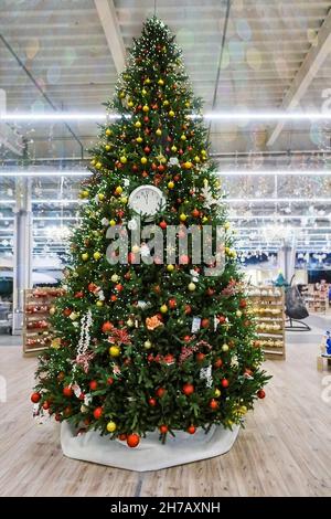 Weihnachtsbaum mit Cloks, bunten Spielzeugen, Girlanden und Lichtern im Laden für die Winterferien geschmückt. Verschwommener Hintergrund mit Pailletten-Girlanden Stockfoto