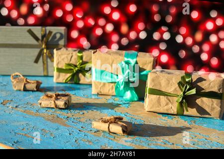 Sieben eingewickelte Vintage Geschenkboxen auf blauem, altem Holzhintergrund. Geschenk-Box in Bastelpapier mit grüner Schleife mit Schatten. Urlaubskonzept. Rot Stockfoto