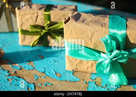 In Nahaufnahme verpackte Vintage-Geschenkboxen mit türkisblauem Bogen auf blauem, altem Holzhintergrund. Geschenk-Box in Bastelpapier mit grüner Schleife. Urlaubskonzept Stockfoto