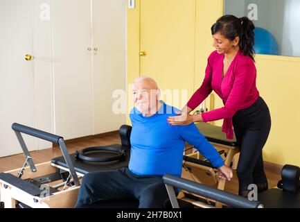 Ein professioneller Trainer hilft einem älteren Mann bei der Wiederherstellung der Gesundheit im Pilates-Kurs Stockfoto