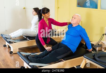 Ein professioneller Trainer hilft einem älteren Mann bei der Wiederherstellung der Gesundheit im Pilates-Kurs Stockfoto