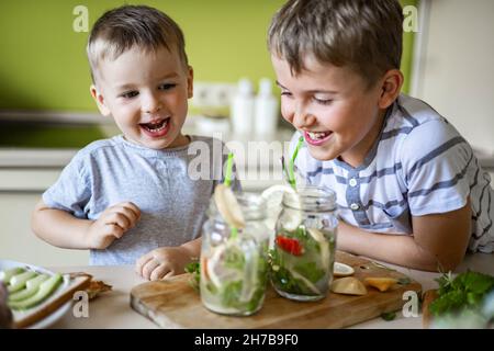 Zwei lachende kleine Jungen trinken erfrischenden Vitamin Sommer Cocktail aus Glas verwenden Stroh Spaß haben Stockfoto