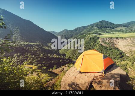 Das orangefarbene Zelt steht auf einer Klippe am Rand einer hohen Klippe in eine Bergschlucht. Gefährliches Lager von Bergsteigern und Bergsteigern in Transkaukasien Stockfoto