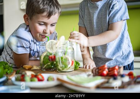 Zwei lachende kleine Jungen trinken erfrischenden Vitamin Sommer Cocktail aus Glas verwenden Stroh Spaß haben Stockfoto