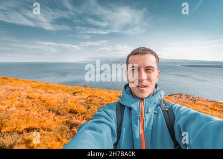 Ein männlicher Reisender macht im indischen Sommer ein Selfie vor dem Hintergrund des Sevan-Sees. Tourismus in Armenien im Herbst Stockfoto