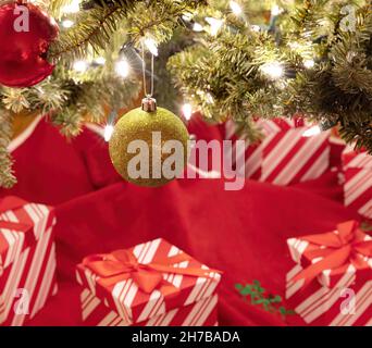 Hängender goldener Kugelschmuck mit hellem Tannenbaum und Geschenken im Hintergrund für ein frohes Weihnachtsfest oder ein glückliches Neues Jahr-Konzept Stockfoto