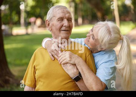 Sportliche ältere Frau umarmt Freund beim Training im grünen Park Stockfoto