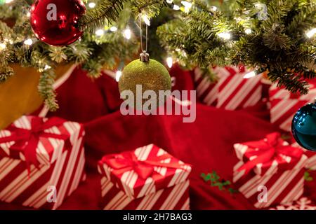 Nahaufnahme einer hängenden goldenen Kugel mit hellem Tannenbaum und Geschenken im Hintergrund für ein „Frohe Weihnachten“- oder „Happy New Year“-Konzept Stockfoto