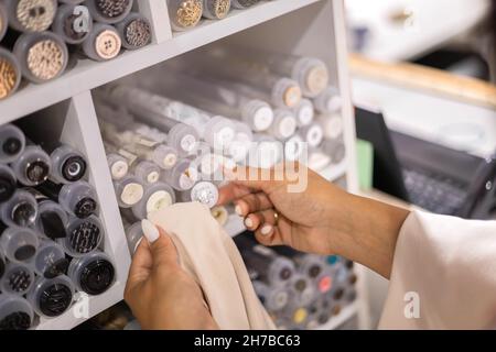 Nahaufnahme Frau Näherin Hände Wahl Knopf Stud zu Gewebeprobe im Geschäft. Schneiderarbeit Stockfoto