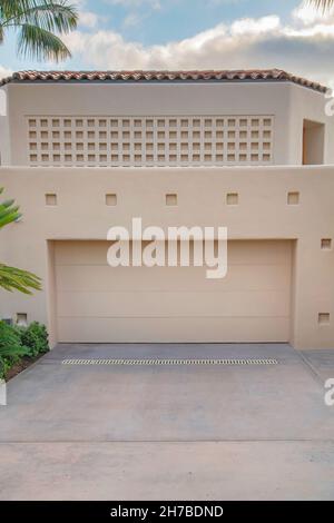 Garage mit beigefarbenen Wänden und Türen im La Jolla, Kalifornien. Moderne mediterrane Garage außen mit Pflanzen und Bäumen außen und einem Quadrat tex Stockfoto