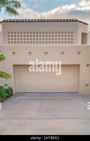 Garage mit beigefarbenen Wänden und Türen im La Jolla, Kalifornien. Moderne mediterrane Garage außen mit Pflanzen und Bäumen außen und einem Quadrat tex Stockfoto