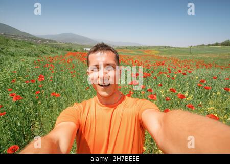 Ein fröhlicher Kerl macht ein Selfie auf einem schönen Mohnfeld auf dem Land Stockfoto