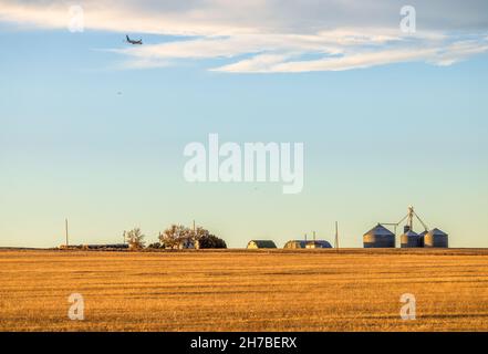 Ein ländliches Bauerngehöft auf einem geernteten Feld auf der Coloradan-Prärie mit den Flugzeugen am Himmel Stockfoto