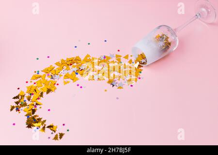 Neujahrskarte. Ein Glas Champagner, Gold funkelt in Form von Weihnachtsbäumen und Sternen, die auf einem rosa Hintergrund aus dem Glas strömen. Vorderansicht. Stockfoto