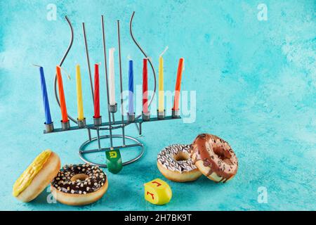 Happy Hanukkah und Hanukkah Sameach - traditioneller jüdischer Kerzenständer mit Kerzen, Donuts und Spinning Tops auf blauem Hintergrund. Inschrift auf Hebräisch Stockfoto