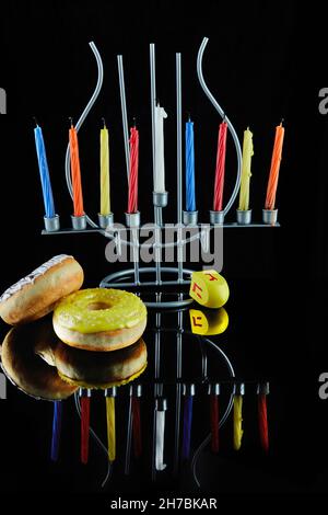 Happy Hanukkah und Hanukkah Sameach - traditioneller jüdischer Kerzenständer mit brennenden Kerzen und Donuts vor schwarzem Hintergrund mit Spiegelung. Stockfoto