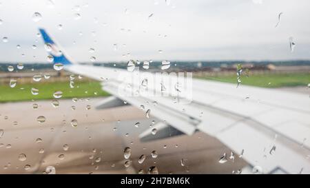 Blick auf einen Flugzeugflügel aus einem mit Wassertropfen bedeckten Fenster. Wasser tropft aus dem Flugzeugfenster von innen Stockfoto