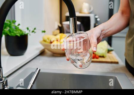 Frau goss Wasser aus dem Wasserhahn in das Glas in der Küche Stockfoto