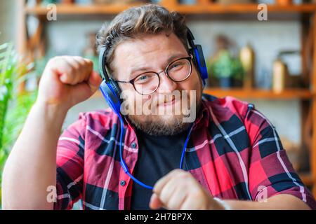 Foto eines jungen Mannes mit Kopfhörern, der zu Hause vor dem Laptop-Monitor arbeitet. Online-Streaming oder Online-Videoanruf. Modernes Technologiekonzept am Vorabend Stockfoto