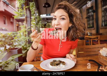 Happy Woman isst Dolma, ein traditionelles armenisches und georgisches Gericht aus Hackfleisch, das in Traubenblätter gehüllt ist Stockfoto