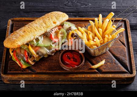 Philly Cheese Steak Sandwich mit gebratenem Rindfleisch, Pfeffer, karamellisierten Zwiebeln, Pilzen und geschmolzenem Käse mit Pommes Frites, Nahaufnahme Stockfoto