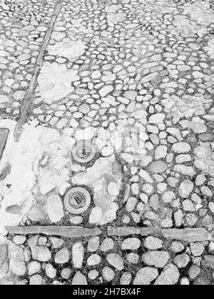 Schwarz-weißes Detail einer alten Straße mit Kopfsteinpflaster und zwei eingebetteten Hydranten in Corte, Korsika, Frankreich Stockfoto