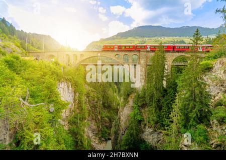 Roter Zug über die Solis Viadukt-Brücke der Schweizer Eisenbahn in der Schweiz nach Pontresina. Schweizer Zug Bernina in Graubünden bei Sonnenuntergang. Albula Stockfoto