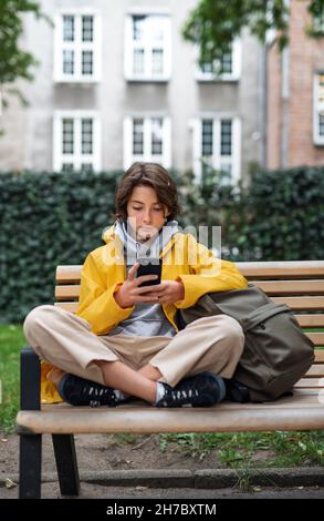 Das Mädchen sitzt auf der Bank und benutzt das Smartphone im Freien in der Stadt. Stockfoto