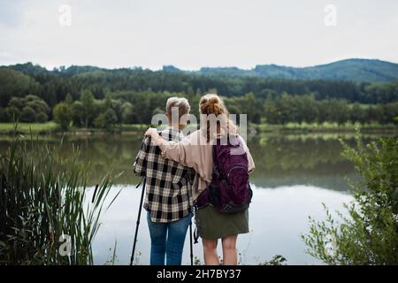 Rückansicht der älteren Mutter, die sich mit der erwachsenen Tochter umarmt, wenn sie im Freien am See in der Natur steht Stockfoto