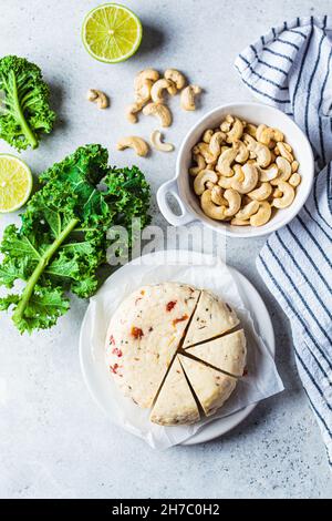 Flacher, veganer Cashew-Käse mit getrockneten Tomaten und Gewürzen, grauer Hintergrund, Draufsicht. Alternative milchfreie Ernährung, pflanzliche Nahrung. Stockfoto