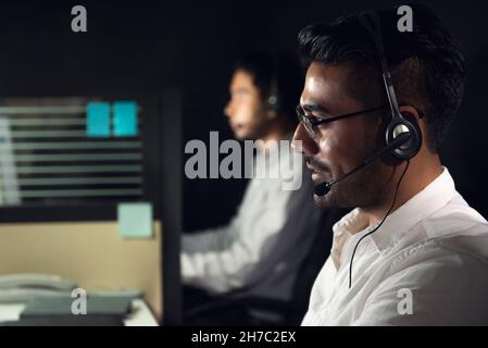 Asiatischer Geschäftsmann, der Nachtschicht im Callcenter-Büro mit einem Kollegen arbeitet Stockfoto