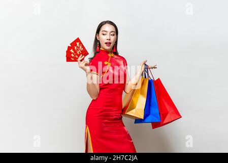 Schöne asiatische Frau in traditionellen orientalischen Kleid hält Taschen und Blick auf rote Umschläge in isolierten hellgrauen Studio Hintergrund für Chinesisch neu Stockfoto