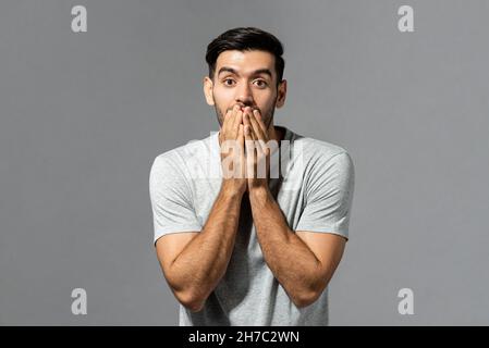 Schockiert überraschenden jungen kaukasischen Mann mit Händen bedeckt Mund in isolierten hellgrauen Studio-Hintergrund Stockfoto