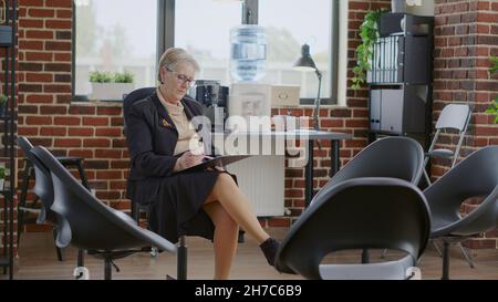 Eine Therapeutin, die auf die Zwischenablage schaut und auf die Leute wartet, die zur Therapiestunde kommen. Psychiater Vorbereitung auf die Rehabilitation Gruppe Treffen mit Patienten, Hilfe bei der sucht. Stockfoto