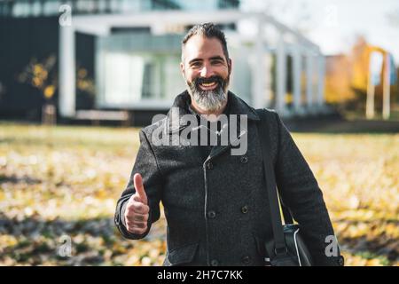 Porträt eines glücklichen Geschäftsmannes, der den Daumen nach oben zeigt. Schwarzer bärtiger Mann lächelt. Stockfoto