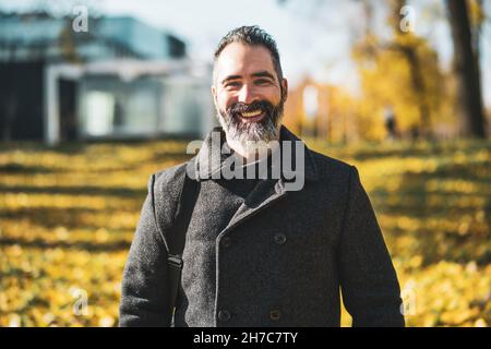 Porträt eines glücklichen Geschäftsmannes im Park im Herbst. Schwarzer bärtiger Mann lächelt. Stockfoto