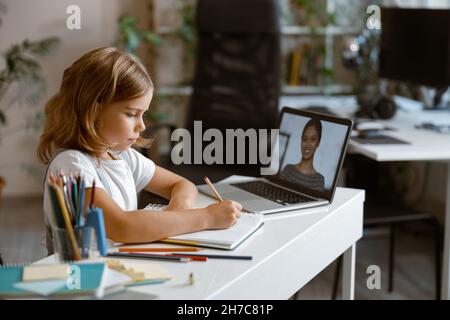 Das kleine Mädchen studiert entfernt am Videocall per Laptop am Tisch im hellen Raum Stockfoto